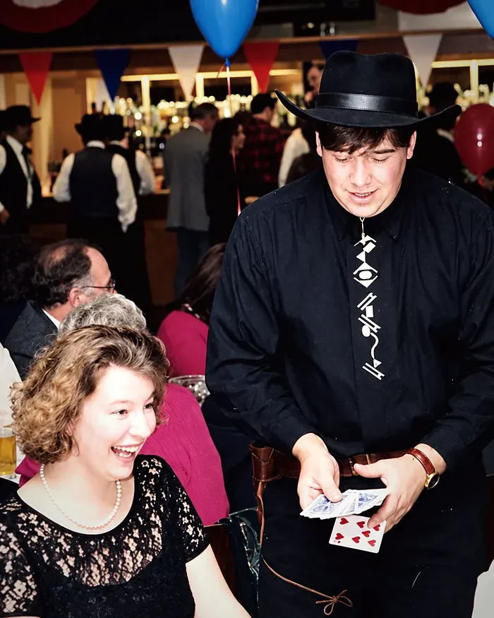 Jonathon in a black shirt and hat, showing cards to a laughing guest at a party